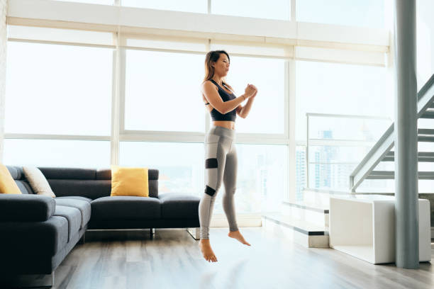 Adult Woman Training Legs Doing Squat and Jumping Fit young Pacific Islander woman training at home. Beautiful female athlete working out for wellbeing in domestic gym, training legs muscles with squats and jumps. woman legs open stock pictures, royalty-free photos & images