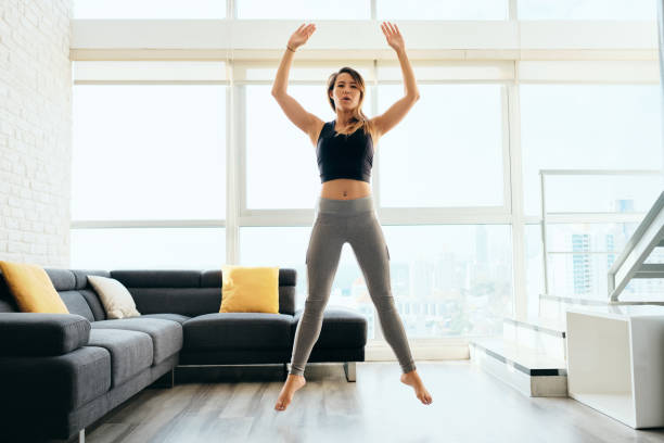 Adult Woman Training Legs Doing Squat and Jumping Fit young Pacific Islander woman training at home. Beautiful female athlete working out for wellbeing in domestic gym, training legs muscles with squats and jumps. woman legs open stock pictures, royalty-free photos & images