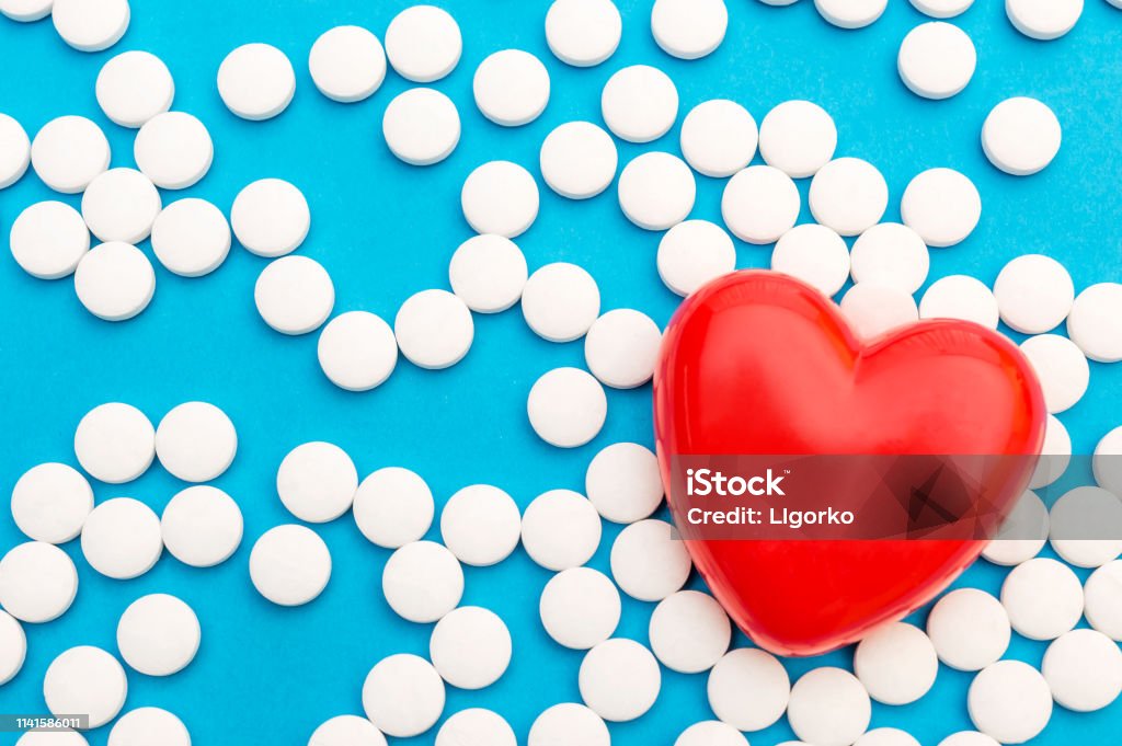 Red heart with white pills on blue. Medical background. Top view. Space for text. Aspirin Stock Photo