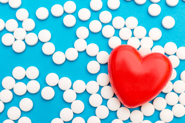 Red heart with white pills on blue. Medical background. Top view. Space for text. Red heart with white pills on blue. Medical background. Top view. Space for text. aspirin photos stock pictures, royalty-free photos & images