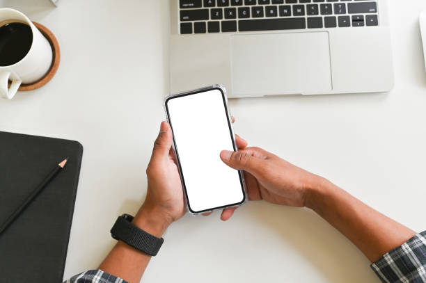 istock Closeup top view man hands using smartphone mockup at the white office desk. Blank screen mobile phone for montage. 1141594712