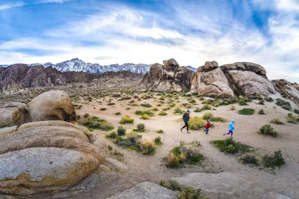 A mother and two children hiking in the Alabama Hills in the eastern Sierra Nevada in California. Lone Pine Peak and Mt. Whitney loom in the distance behind.