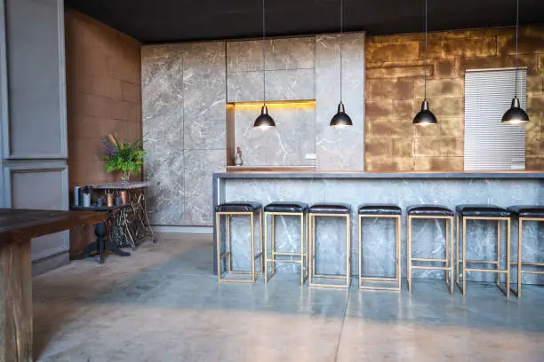 Photo of Industrial loft bar style.  The room has a lot of chairs at the bar ,four overhanging lamps, marble table