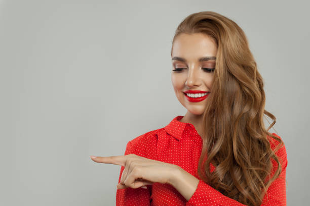 istock Attractive model with makeup and long curly hair pointing aside and smiling on white background 1141606542