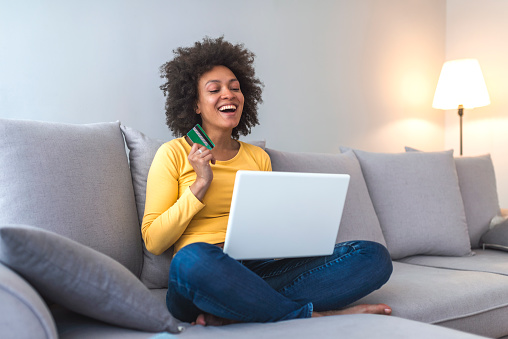 Girl doing e-shopping. Woman with computer shopping online. Young confident pretty woman working with laptop and credit card at home. Woman on couch with credit card and laptop