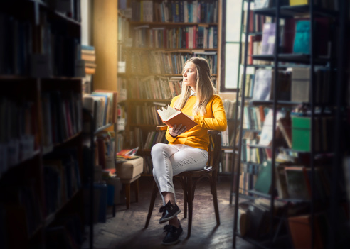 Young woman reading in the library with beautiful light from a window