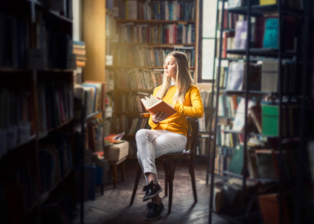 young woman reading in the library - adult education full length book imagens e fotografias de stock