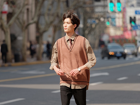 Portrait of a handsome Chinese young man with Korean style clothes walking on street in hurry in sunny day, male fashion, cool Asian young man lifestyle.