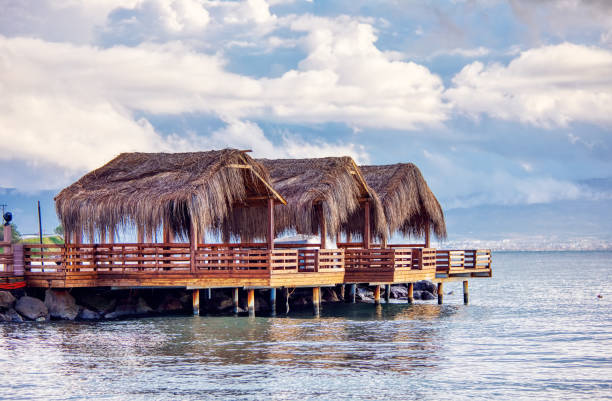 istock Three beach huts with palm leaf covered roofs on a wooden platform over the sea at sundown. Beautiful seascape and cloudscape view. 1141639066