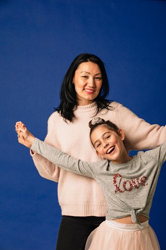 Portrait of a young girl and her mother laughing and having fun. The mother is holding her daughters arms above her head.