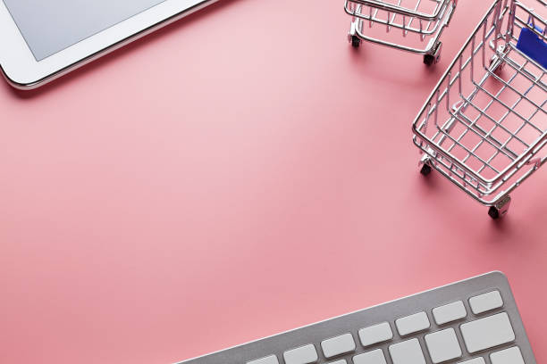 Shopping carts, computer keyboard and modern tablet on pink background stock photo