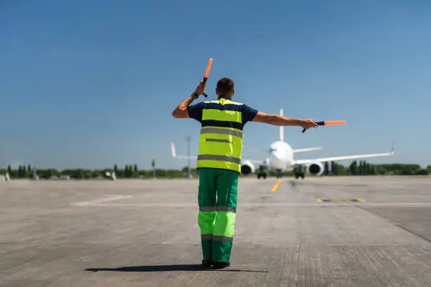 Time for landing. Aviation marshaller meeting passenger plane at the airport