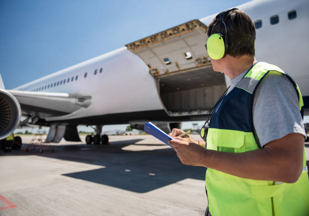 istock Airport worker looking at passenger plane while holding clipboard and pen 1141642758