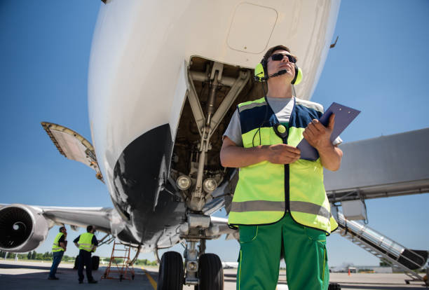 istock Airport worker with clipboard standing in front of plane while colleagues working 1141642767