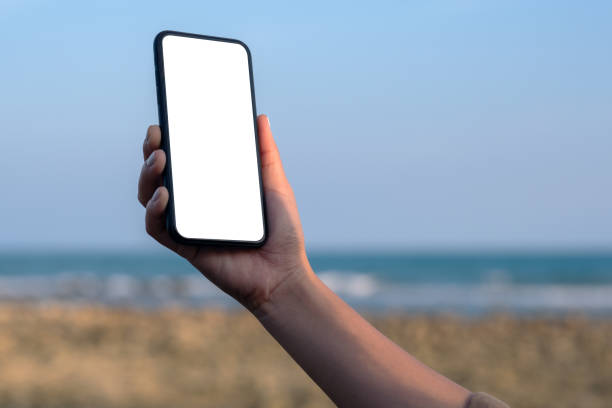 istock Mockup image of woman's hand holding black mobile phone with blank desktop screen by the beach and sea with blue sky background 1141645749