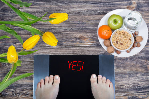 Digital scales with female feet on them and sign yes! surrounded by spring flowers, plate with healthy food and glass of wate stock photo