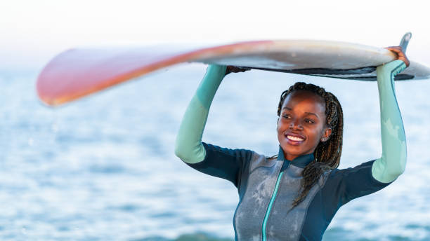 istock Smiling african woman holding a surfboard over her head. 1141649464