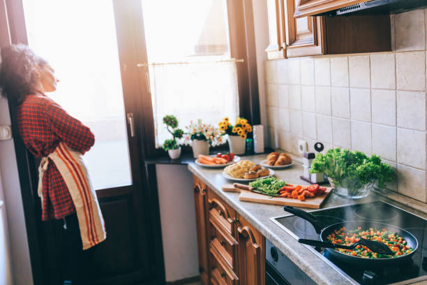 istock Pensive woman standing in kitchen and looking through window 1141649479