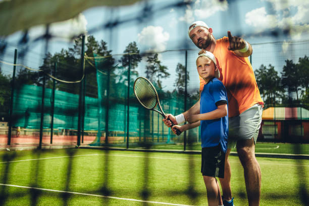 Focused man and child on field Portrait of concentrated male trainer teaching serene boy playing tennis outdoor. He pointing hand tennis coach stock pictures, royalty-free photos & images