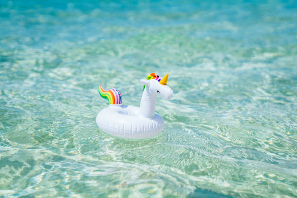 istock Inflatable white unicorn floating at transparent turquoise sea. Blue sky with few clouds on the background. 1141651921