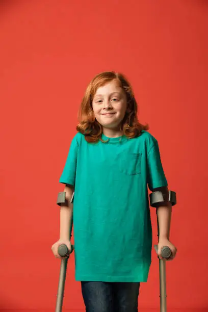 A young boy standing in a studio, using crutches for support.