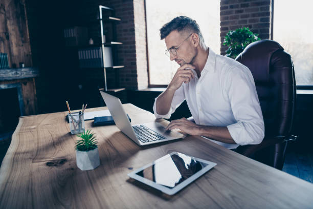 fechar perfil lateral até foto bonito ele ele seu cara macho ponderar pensativo ter em linha de negócios moeda bate-papo cartas atento notebook mesa sentar-se grande escritório cadeira desgaste especificações formal-vestir camisa branca - technology contemplation clothing formalwear - fotografias e filmes do acervo