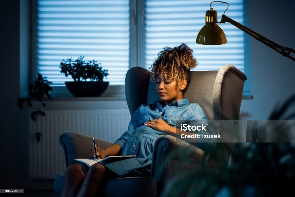 Pregnant businesswoman writing on book in office Pregnant businesswoman writing on book. Female expertise is relaxing on armchair in new office. She is wearing business casuals. Pregnant Stock Photo
