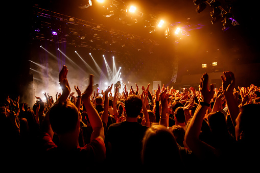 Multitud en show musical, gente feliz con manos levantas. Luz de escenario naranja. photo