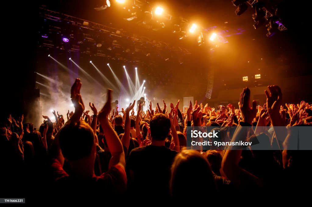 Multitud en show musical, gente feliz con manos levantas. Luz de escenario naranja. - Foto de stock de Actuación - Representación libre de derechos