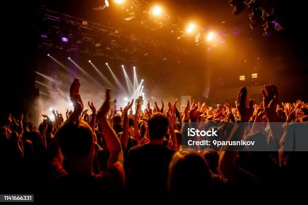 Multitud En Show Musical Gente Feliz Con Manos Levantas Luz De Escenario Naranja Foto de stock y más banco de imágenes de Actuación - Representación