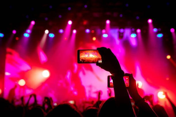 smartphone en mano en un concierto, luz roja del escenario - concierto fotografías e imágenes de stock