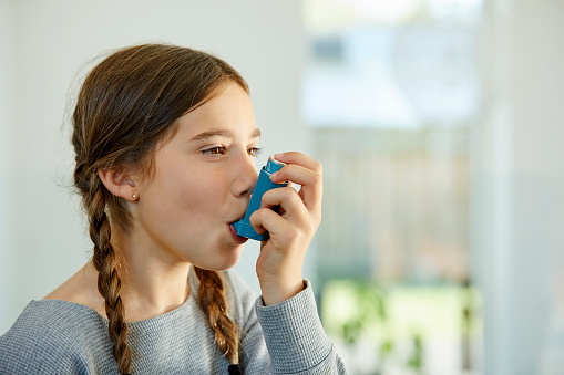 Close-up of girl using asthma inhaler at home. Little girl is suffering from health issues. She is looking away while taking dose.