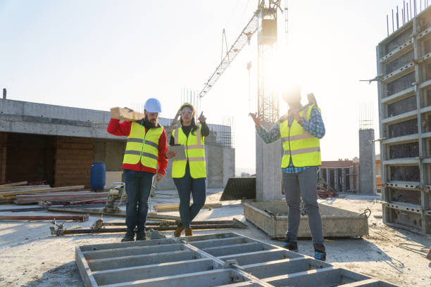 istock WS, Meeting of a Confident Female Architect, A Project Manager and a Construction Workers Discussing and Working Together at Construction site of a Residential Building on a Bright Sunny Day Using Architectural Drawings and a Digital Tablet 1141670060