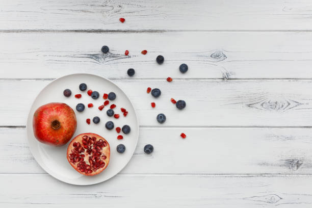 blueberries and pomegranate on a plate on distressed white wood