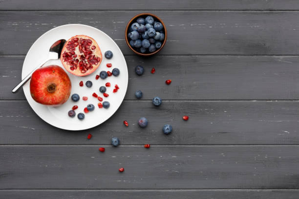blueberries and pomegranate with a silver spoon on a plate on dark grey wood blueberries and pomegranate with a silver spoon on a plate on dark grey wood
