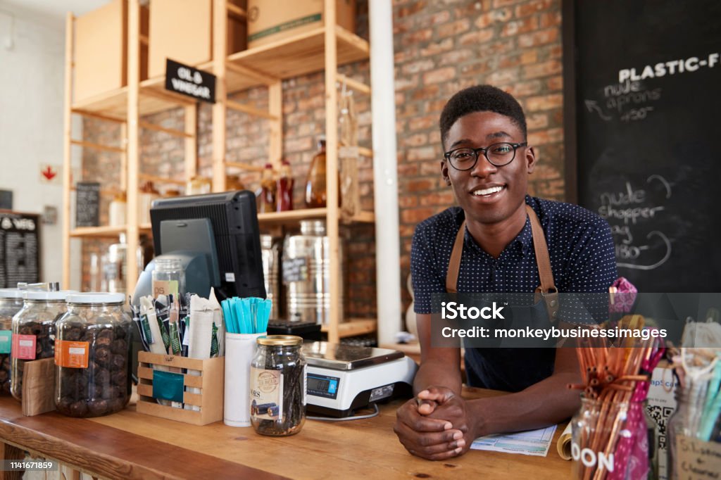 Portrait Of Male Owner Of Sustainable Plastic Free Grocery Store Behind Sales Desk Owner Stock Photo