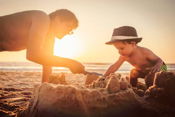 glücklicher kleiner junge und sein vater bauen sandburg am strand - lifestyles child beach digging stock-fotos und bilder