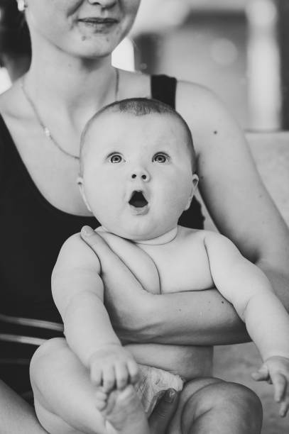 maman tenant bébé fille 6 mois, un bébé dans ses bras à la piscine. la première leçon de natation. préparez-vous à plonger. surpris. avec une bouche ouverte. cheveux roux. close-up.  noir et blanc - family mouth open vertical mother photos et images de collection