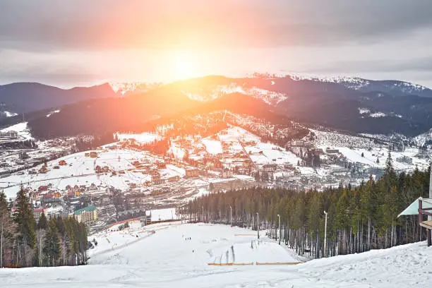 Photo of Panorama of ski resort, slope, people on the ski lift, skiers on the piste among green pine trees and snow lances.