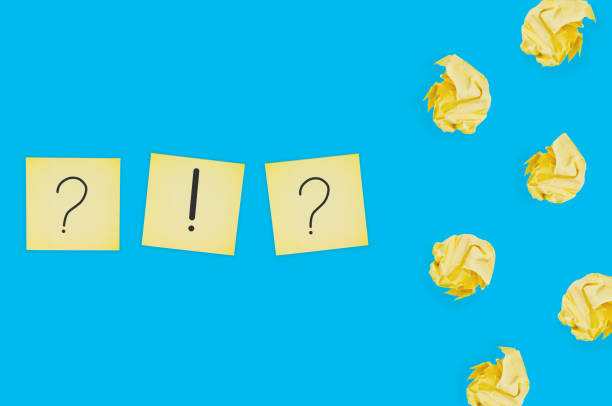 istock Three square paper sheets with handwritten question and exclamation marks near lot of scattered crumpled paper balls on blue table. Top view. Business concept 1141680155