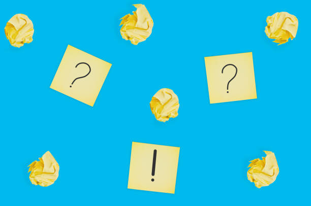 istock Three square paper sheets with handwritten question and exclamation marks near lot of scattered crumpled paper balls on blue table. Top view. Business concept 1141680159