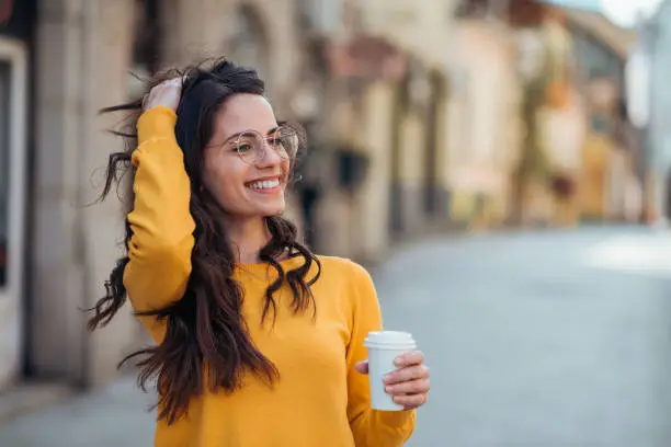 Photo of Gorgeous casual brunette in the town street, smiling and drinking coffee to go.