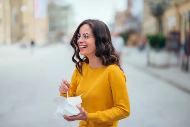 Girl with takeaway box laughing on the street.