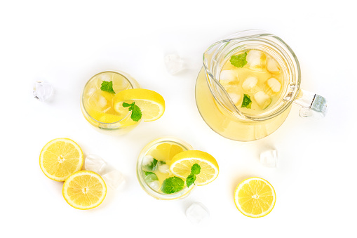 Homemade lemonade in glasses and a jar, with fresh lemons, mint, and ice cubes, shot from the top on a white background with copy space