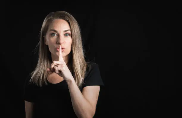 blond woman on a black background. 45-year-old woman trying to keep a secret or make the sign of silence.
