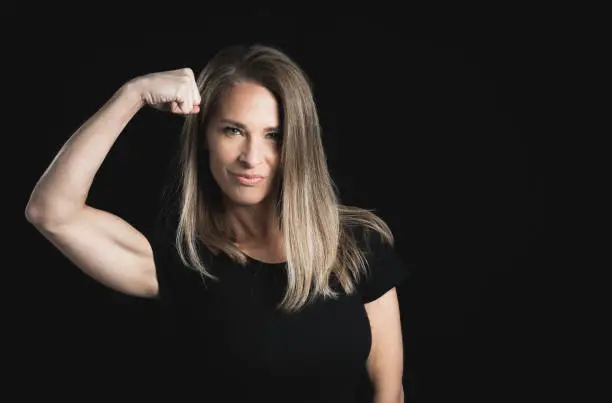 blond woman on a black background. Strong 45 year old woman showing her biceps