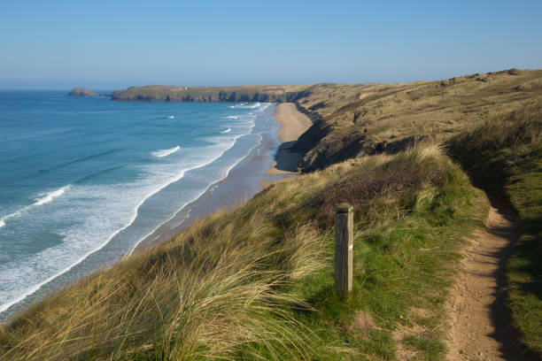 The beach and town are a very popular summertime tourist destination. There is thrift in the foreground and the beach is quiete at low tide. There are buildings of the town behind the beach and on the hillside.