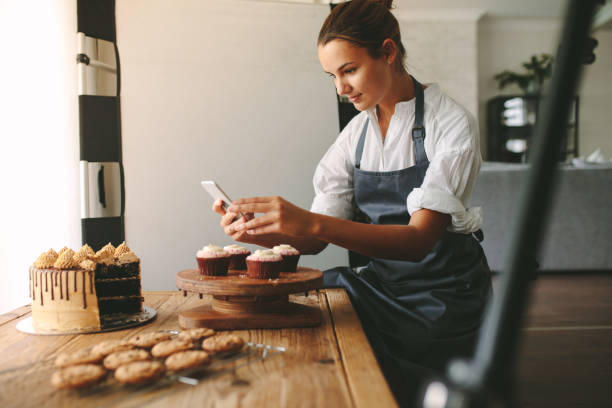 Confectioner photographing pastries Young woman taking pictures of a cake in the kitchen. Female baker capturing photos of pastry items with her mobile phone. confectioner photos stock pictures, royalty-free photos & images