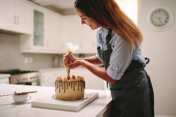 Woman piping decoration on a cake Female chef decorating cake with whipped cream using party bag. Woman in apron preparing a delicious cake at home. bakery photos stock pictures, royalty-free photos & images