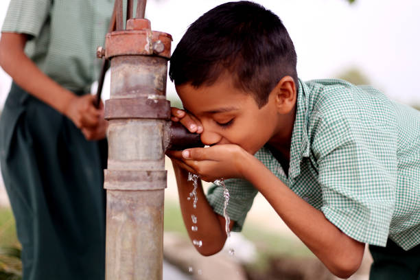 bambino assetato che beve acqua sulla pompa dell'acqua - povertà asia foto e immagini stock